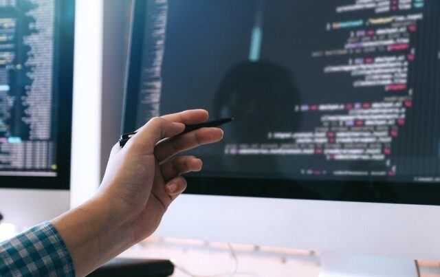 hand pointing to computer screen with computer code