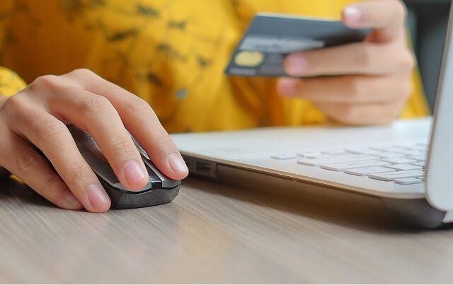 Person using a computer mouse and holding a credit card for online shopping.
