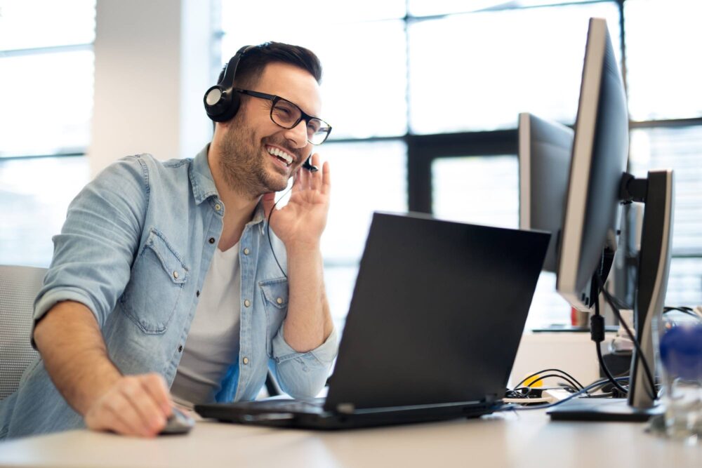 man smiling with headset on laptop