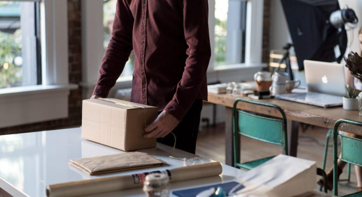 person with tan shipment box and shipping supplies on counter preparing package