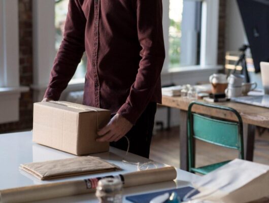 person with tan shipment box and shipping supplies on counter preparing package