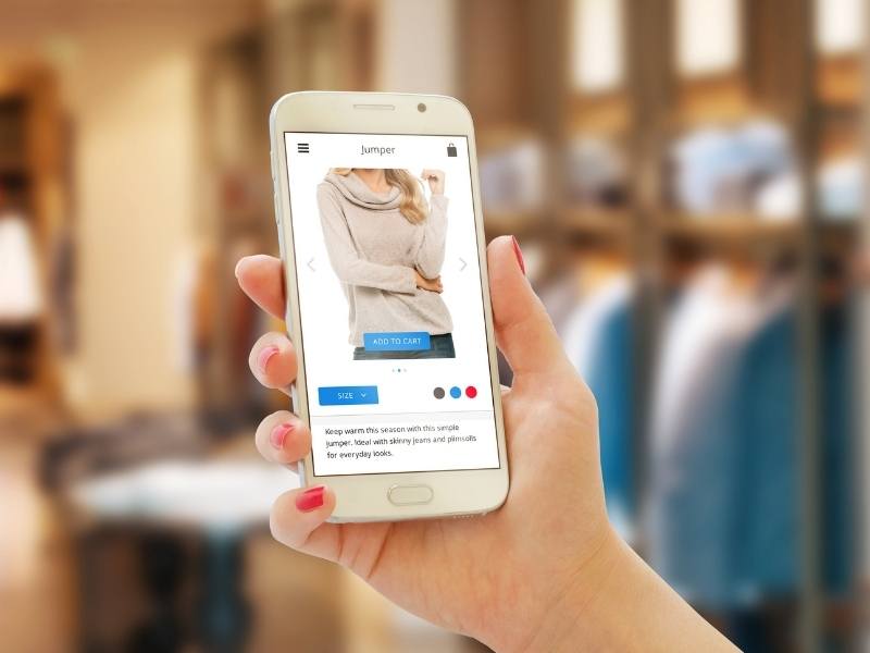 Woman online shopping with smart phone. Clothing store in the background. Shopify SEO optimization.