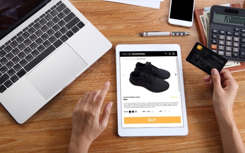 woman using credit card for buy black running shoes on ecommerce website via tablet with laptop, smartphone and office stationery on wooden desk - Enterprise SEO Ecommerce