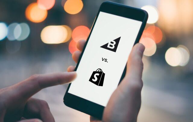 person holding mobile phone showing bigcommerce vs. shopify logos on screen