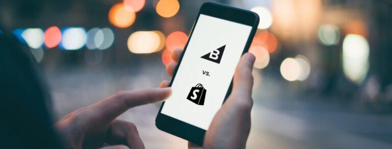 person holding mobile phone showing bigcommerce vs. shopify logos on screen